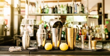 A bartop with a variety of bartender tools, including shakers, a strainer and a jigger. 
