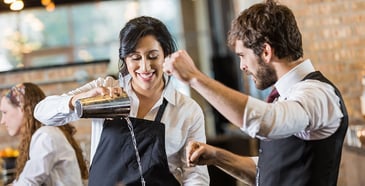 An alcohol server demonstrates to another alcohol server how to pour a drink