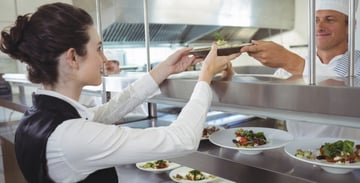 Chef passing plate of food to server