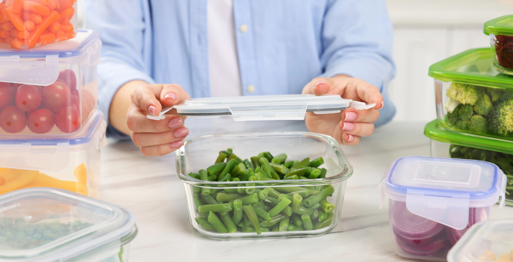 Woman sealing container with green beans at white marble table in kitchen, closeup. Food storage 