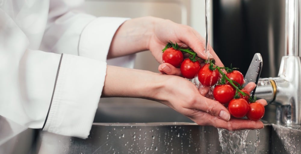 A food handler washes vine tomatoes in the sink